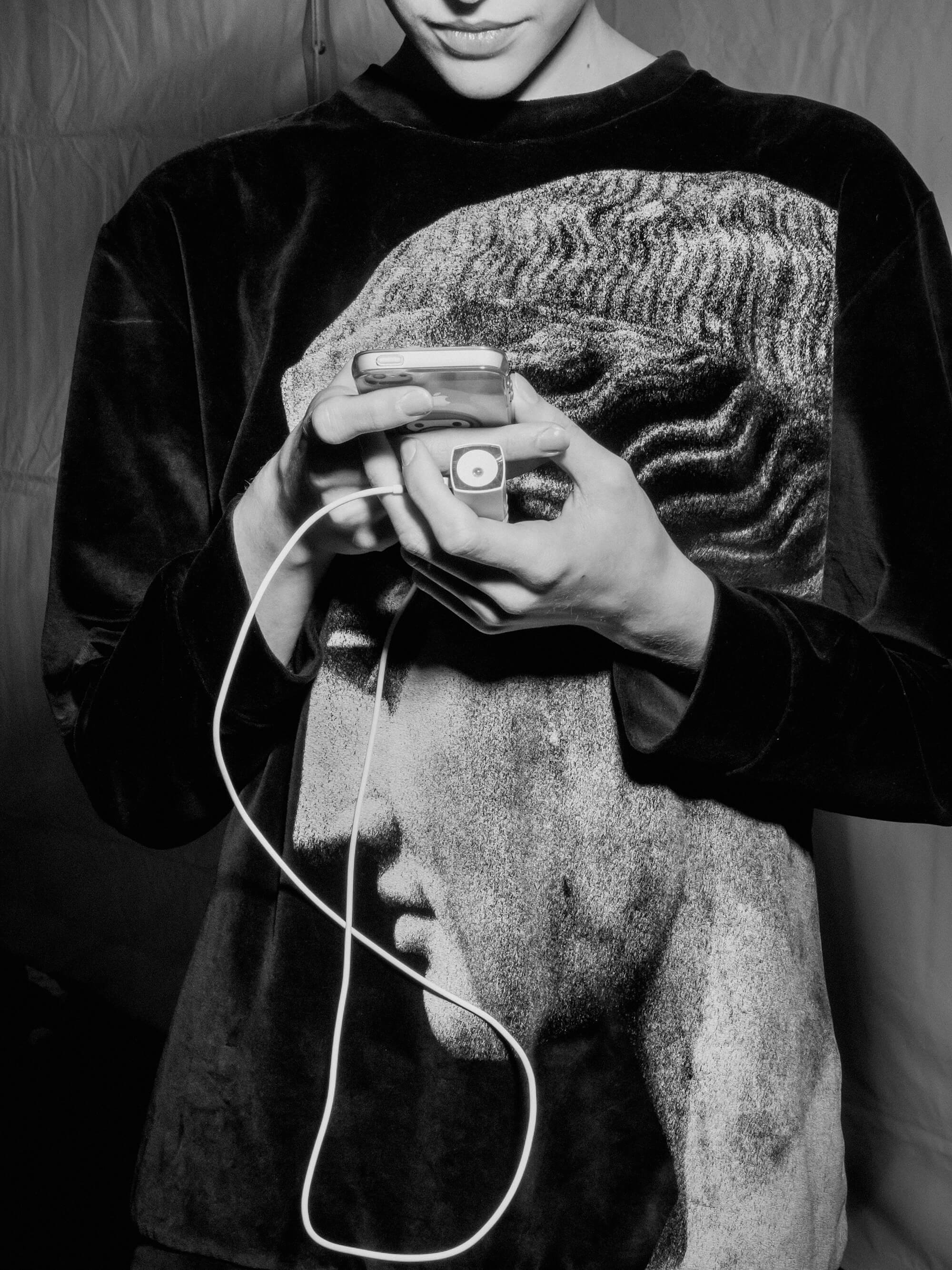 Porträt einer Frau, die ein Sweatshirt mit griechischem Skulpturendruck trägt und ein Handy hält, das mit der Powerbank verbunden ist.